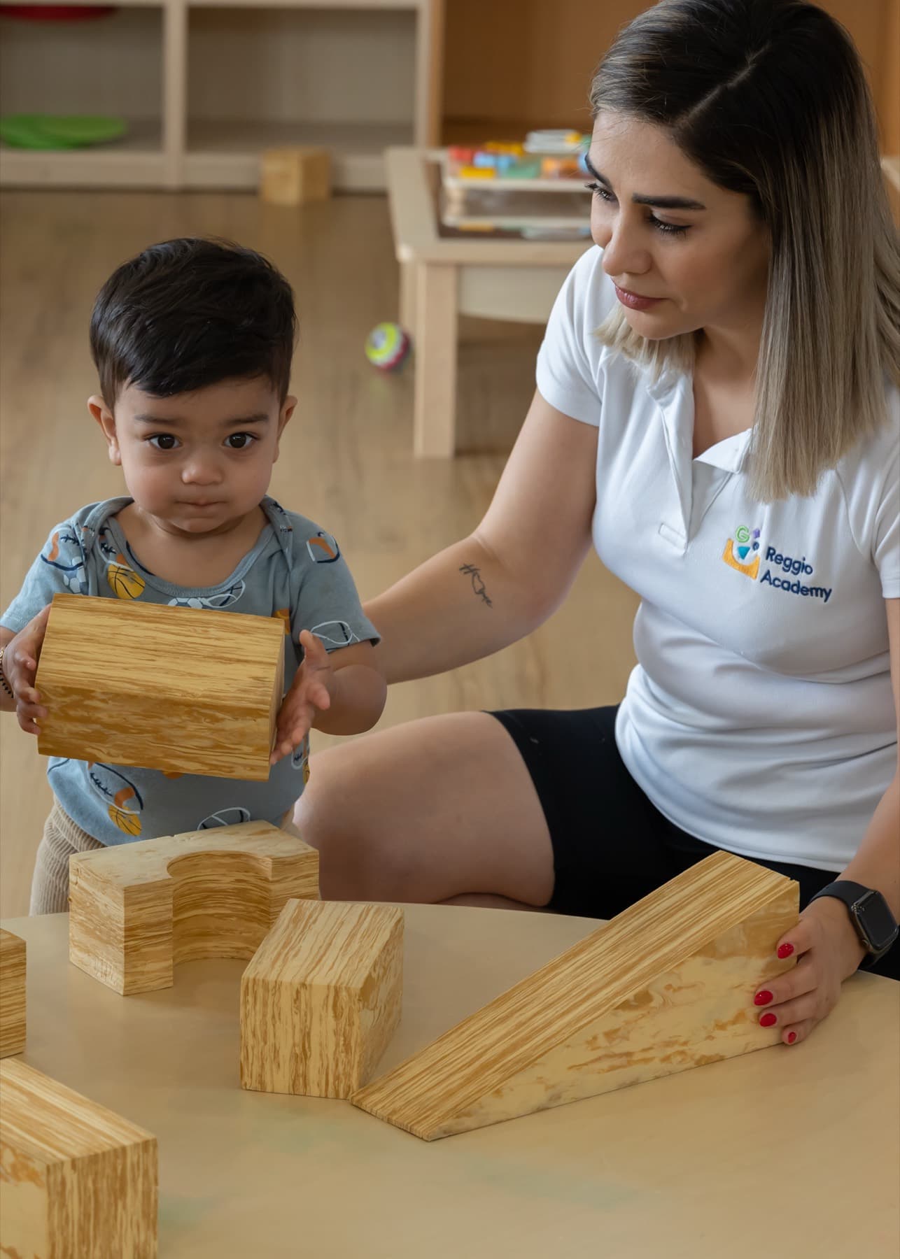 An educator playing with timber blocks alongside a toddler