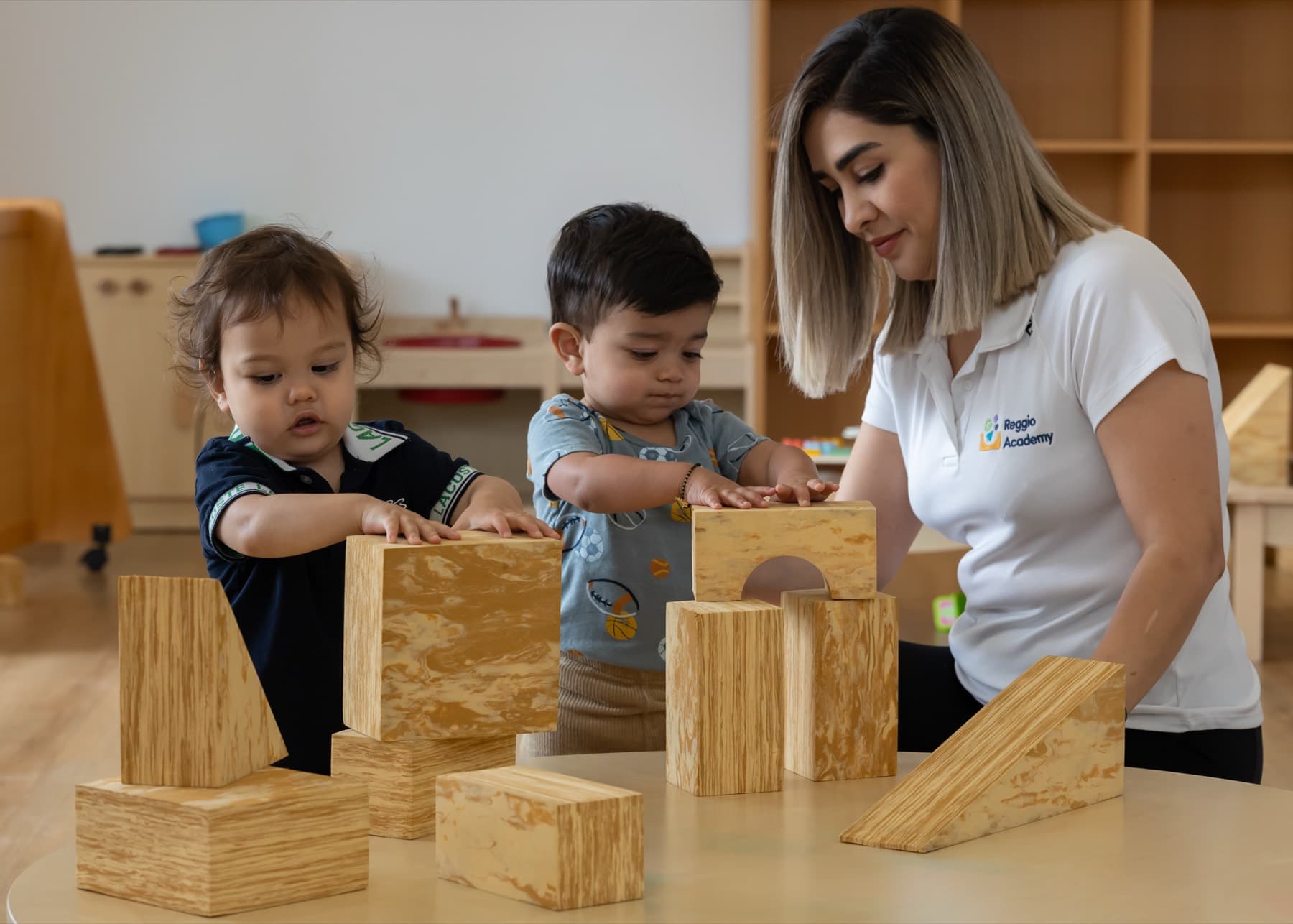 An educator building with timber blocks alongside two toddlers
